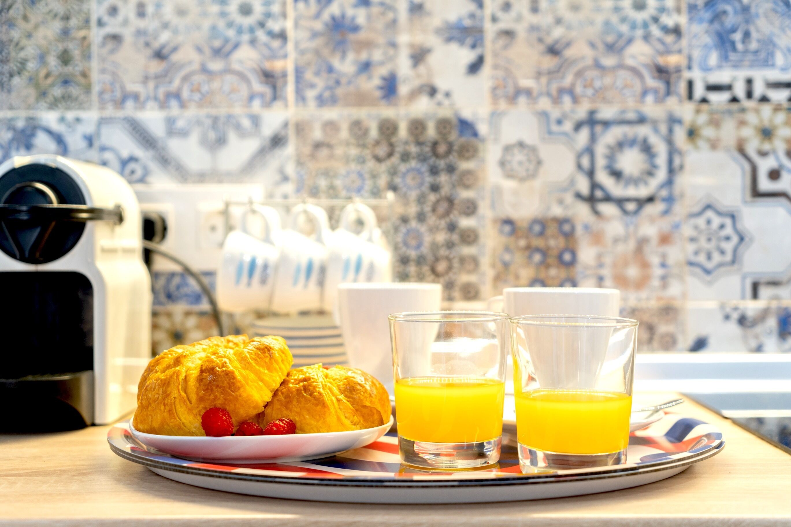 Ein Frühstücksbrett mit Croissants und Orangensaft auf einem Tisch mit Fliesenwand.