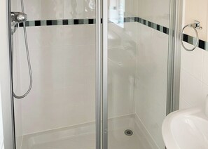A glass-enclosed shower with a chrome showerhead and a drain.