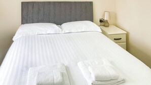Un lit bien fait, avec des draps blancs et deux serviettes pliées posées au pied du lit.