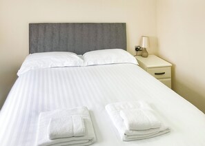 A neatly made bed with white linens and two folded towels on the foot of the bed.