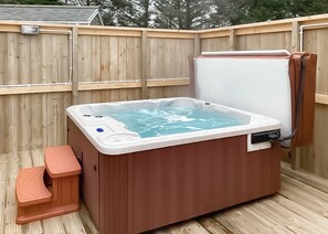 A hot tub with a control panel, a built-in seat, and a wooden deck.