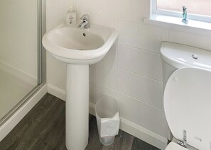 A bathroom with a white sink, toilet, and a window above the toilet.