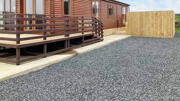 Une cabane en bois dotée d’une terrasse, d’une clôture en bois et d’un sol en gravier.