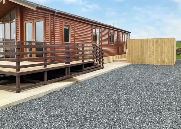 A wooden cabin with a deck, a wooden fence, and a gravel ground.