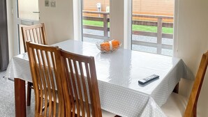 Une table à manger recouverte d’une nappe blanche, des chaises en bois, un panier contenant un objet orange et une télécommande.