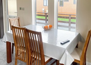 A dining table with a white tablecloth, wooden chairs, a basket with an orange item, and a remote control.