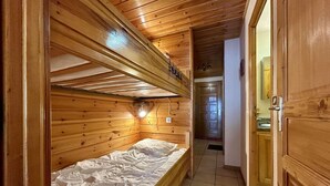 Een houten cabinemeubilair met een stapelbed, een klein raam en een gang naar een badkamer.
