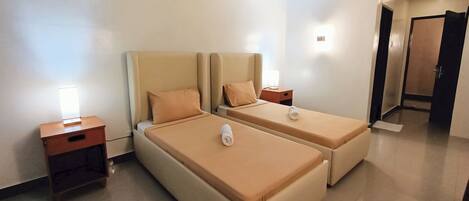 Quarto de hotel com duas camas, cada uma com cabeceira, mesas de cabeceira e uma luminária.