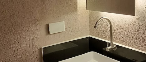 Baño con lavamanos blanco, encimera negra y pared con textura.