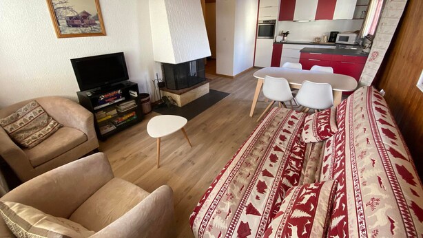Ein Wohnzimmer mit einer Couch, einem Fernseher, einem Kamin, einem Esstisch mit Stühlen und einer Küchenzeile.