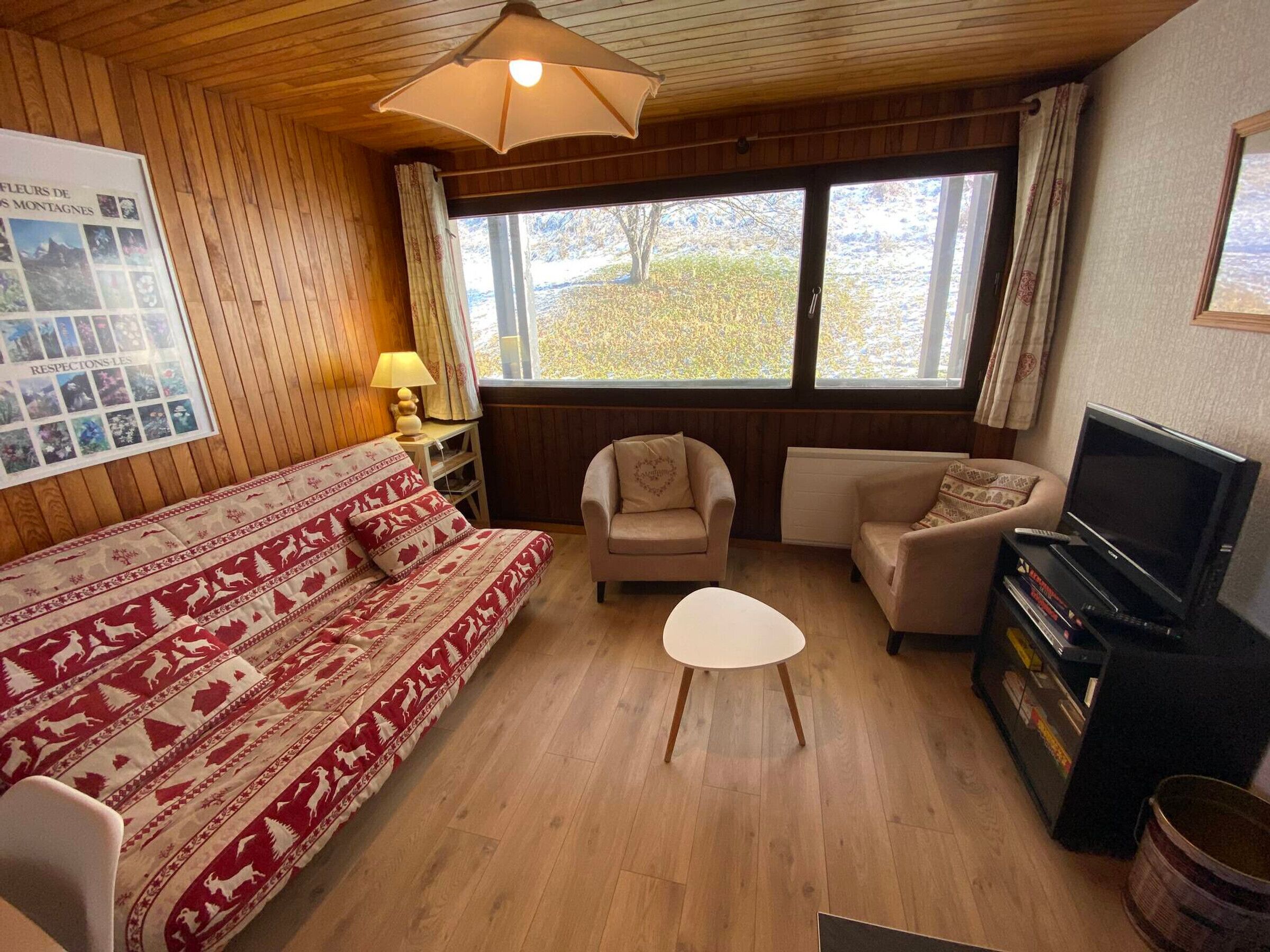 A cozy room with a bed, two sofas, a small table, a TV, and a window with a view of trees.