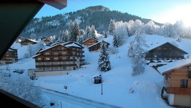 Un pueblo cubierto de nieve con edificios de madera, cielo despejado y una montaña al fondo.