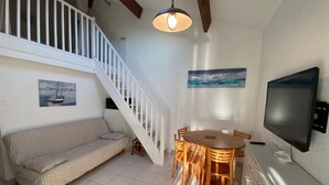 A cozy living room with a sofa, a dining table with chairs, a TV, and a staircase. - Spacious Villa T2 + Mezzanine, AC, 6 Guests, Terrace, Parking, Close to Beach, Port Leucate (Port Leucate)
