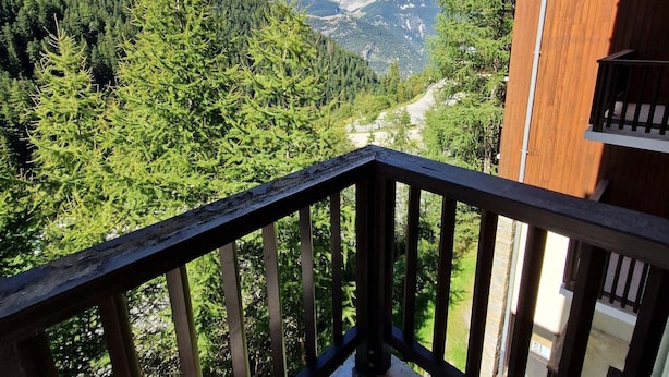 Un balcon en bois offrant une vue sur une vallée boisée et, au loin, sur des montagnes.