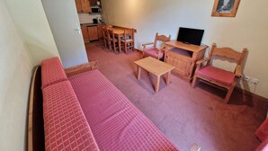 Un espace de vie compact comprenant un canapé, une petite table, un téléviseur et un coin repas.
