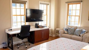 A bedroom with a bed, a desk with a chair, a TV, a sofa, and windows. - Historic St. Augustine Balcony Suite with Parking (Saint Augustine)