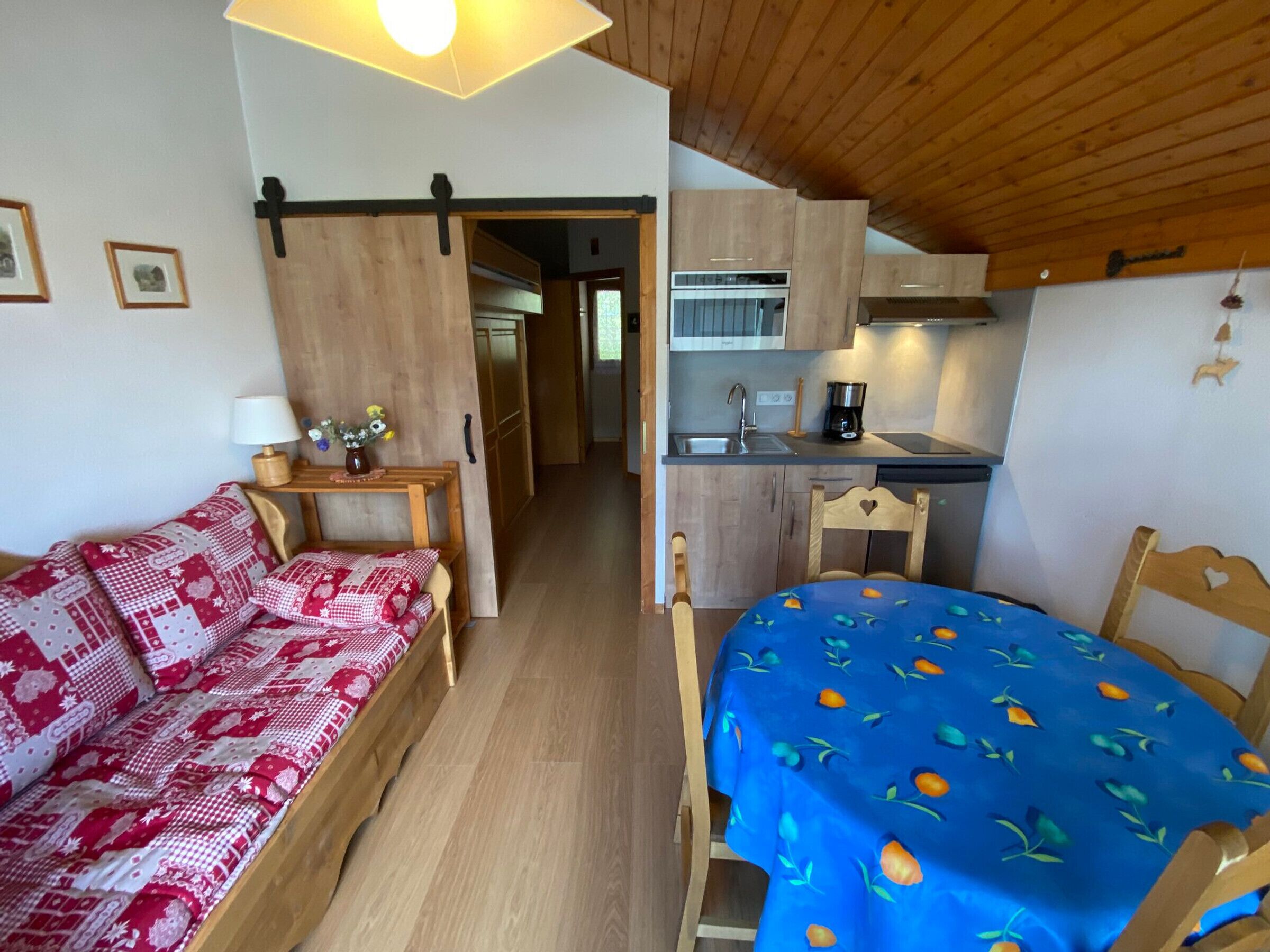 Une pièce chaleureuse avec un canapé en bois, une table à manger recouverte d’une nappe bleue et un coin cuisine.