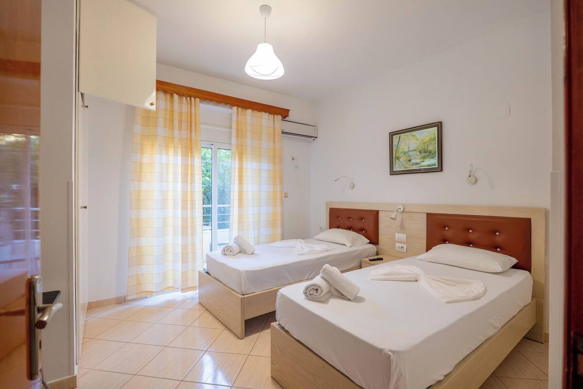 A hotel room with two beds, a wooden headboard, a painting on the wall, and a window with curtains.