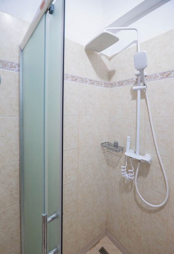 Une douche avec une porte en verre, un pommeau de douche à main et un flexible de douche.