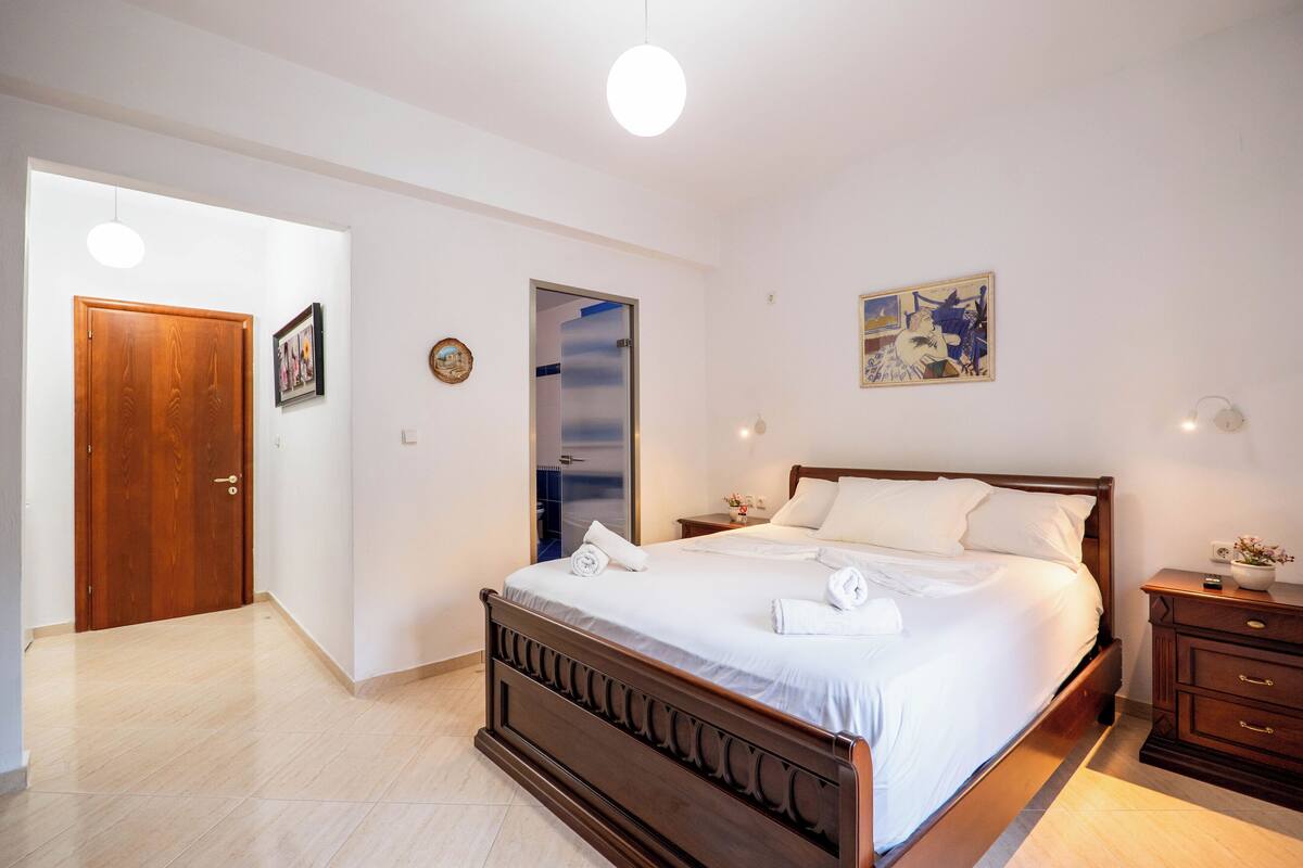 A bedroom with a wooden bed, a nightstand, a wall clock, and a door.