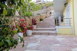 A stone staircase leading to a building with a yellow exterior, surrounded by potted plants and a stone wall. - Sunny Holiday (Sarandë)