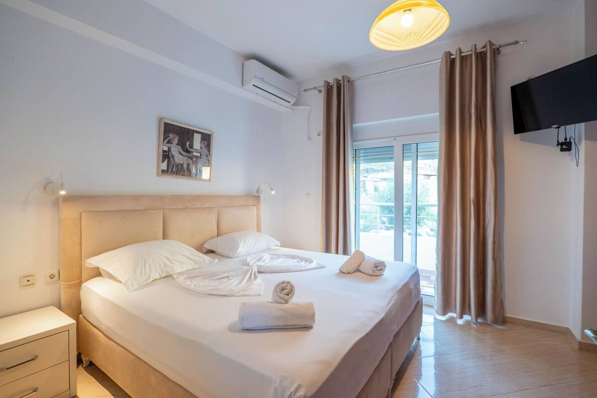 A hotel room with a bed, a flat-screen TV, a painting, and a window with curtains.