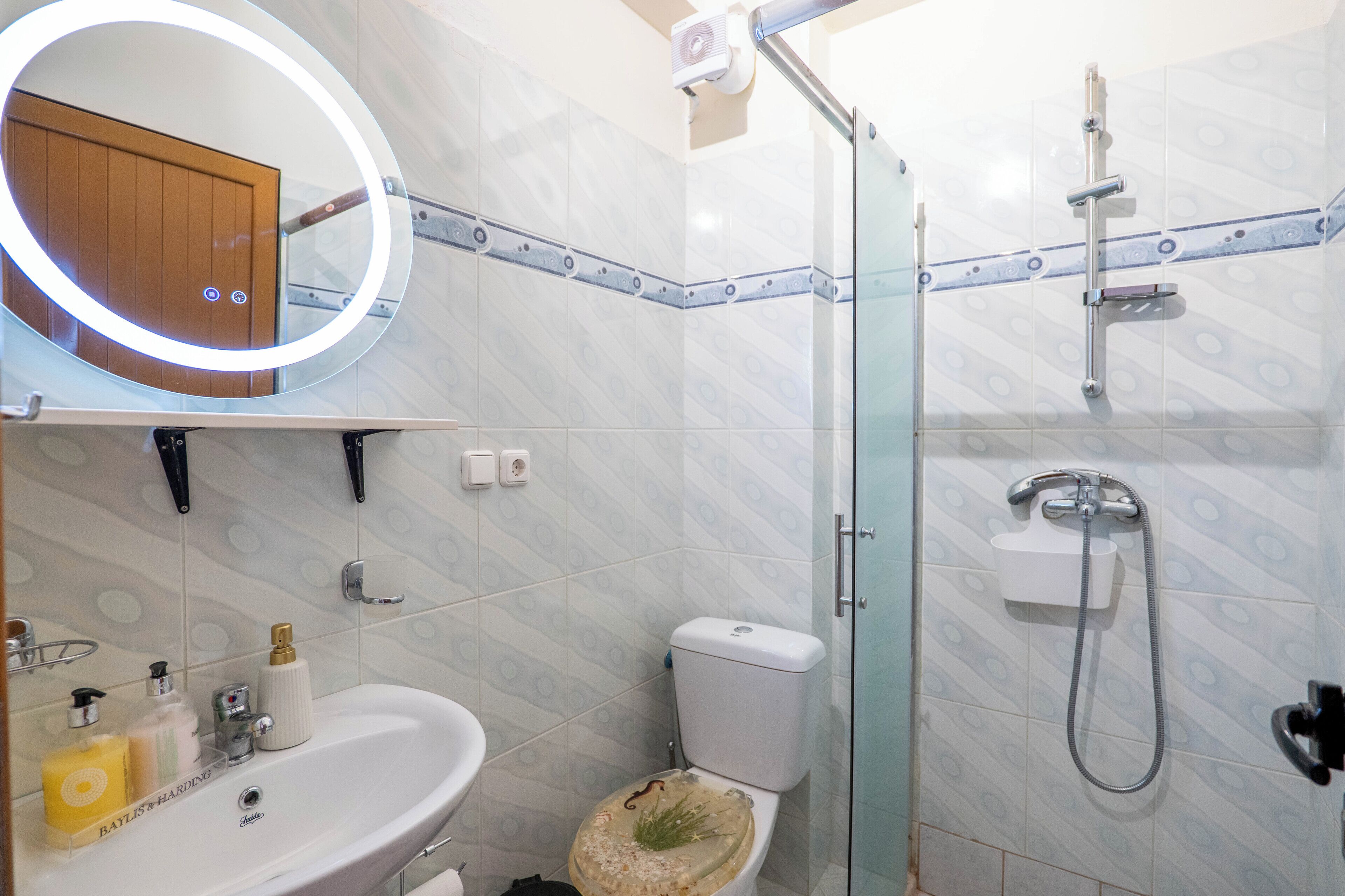 Ein Badezimmer mit Toilette, Waschbecken, Dusche und einem beleuchteten Spiegel.