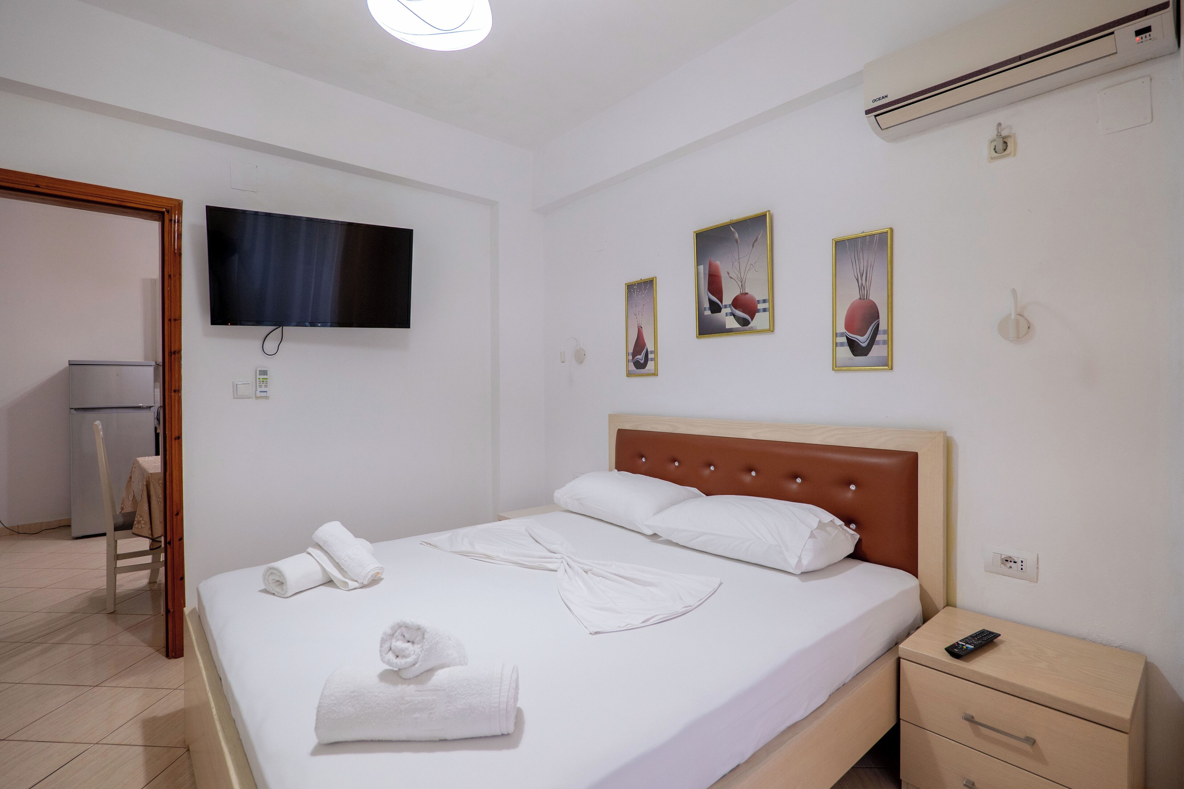 Una camera d'hotel con un letto, una TV a muro, un comodino con un telecomando e opere d'arte alle pareti.