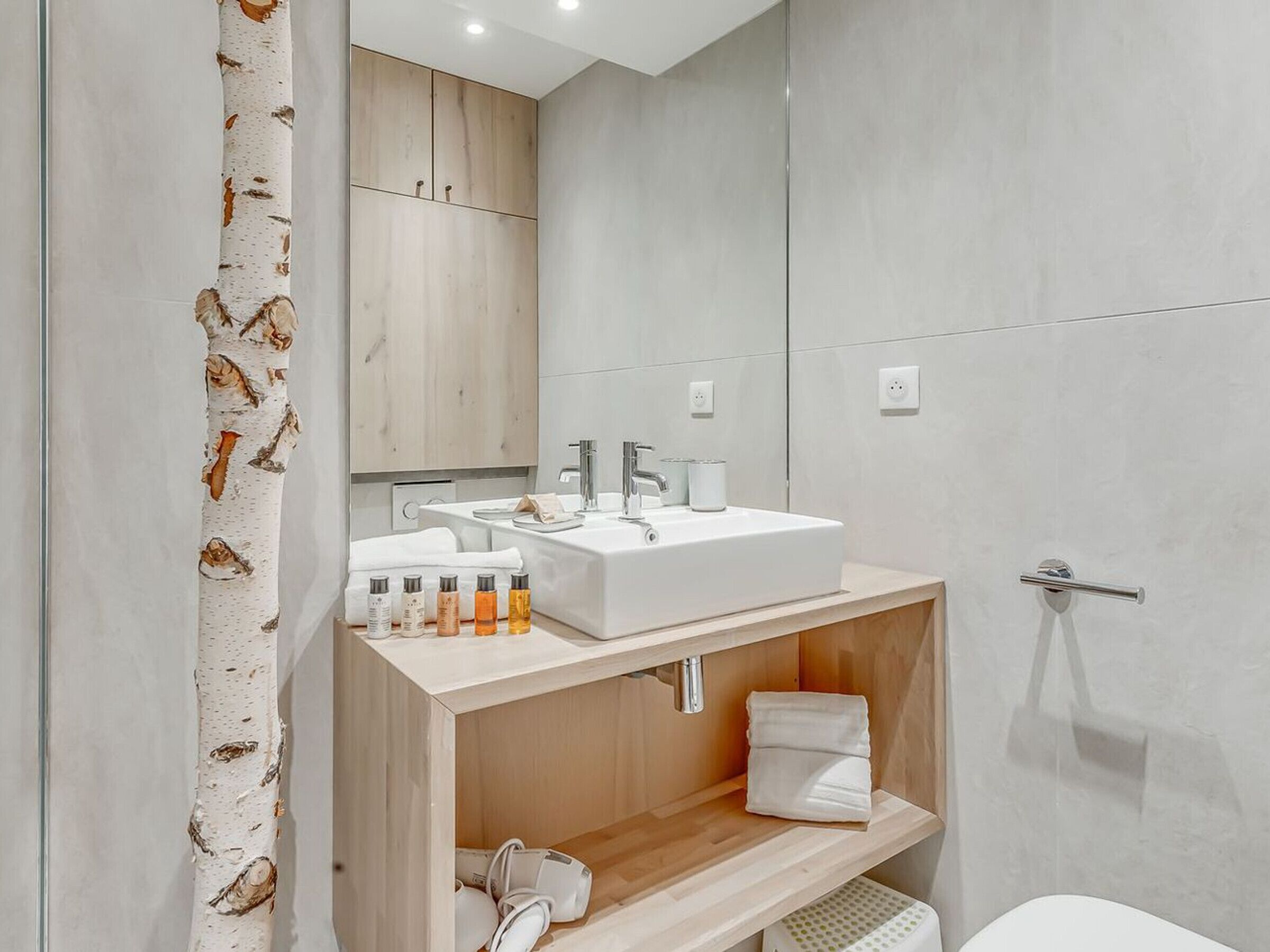 A modern bathroom with a wooden vanity, a large mirror, and a white sink.