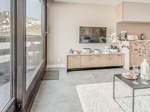 A modern kitchen with a large window, a flat-screen TV, and a dining area with a white rug.