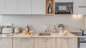 Uma cozinha moderna com armários de madeira clara, micro-ondas embutido, pia e diversos eletrodomésticos.