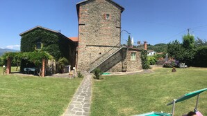 A stone building with a staircase leading to a second floor, surrounded by a well-maintained lawn and a small garden with flowers. - La Casatorre di Ponticello. Casale di campagna con ampio giardino e piscina (Cantiere-ponticello)