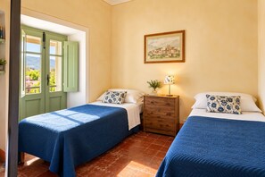 A room with two beds, a wooden nightstand, a framed picture on the wall, and a window with green shutters. - La Casatorre di Ponticello. Casale di campagna con ampio giardino e piscina (Cantiere-ponticello)