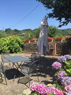 Un patio al aire libre con una mesa y sillas, rodeado de plantas y flores en macetas.