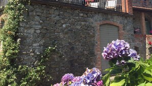 A stone building with a balcony adorned with hanging flower pots. - La Casatorre di Ponticello. Casale di campagna con ampio giardino e piscina (Cantiere-ponticello)