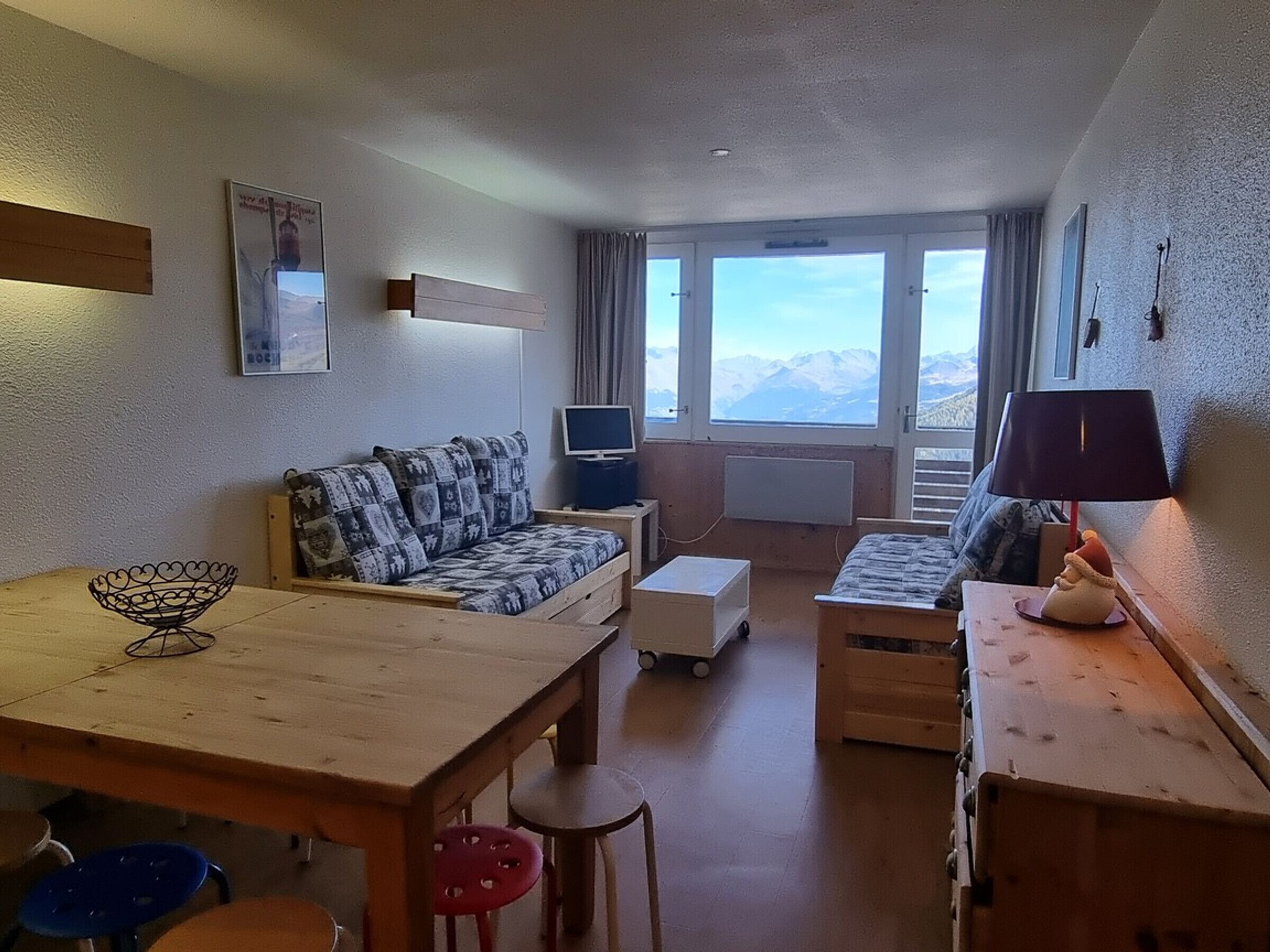Een gezellige woonkamer met een bank, een klein tafeltje en een televisie. Grote ramen bieden uitzicht op de bergen.