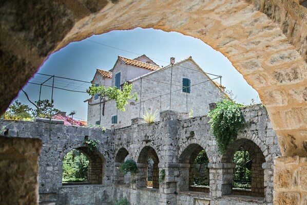 An ancient stone building with arched windows and a tiled roof, viewed through a stone archway.