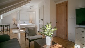 Ein modernes, gut beleuchtetes Zimmer mit Holzboden, einem Bett, einem Fernseher und einer Pflanze auf einem Tisch.