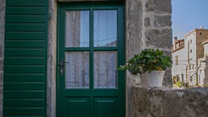 Ein Steinhaus mit grüner Tür und Fensterläden, einem Blumentopf und einer Laterne auf dem Boden.