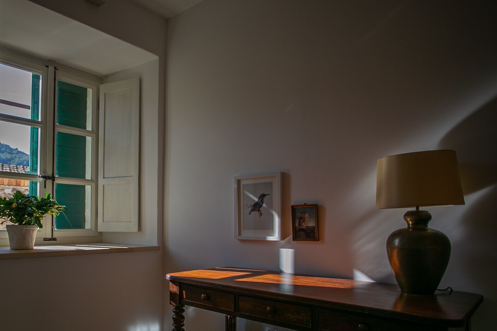 Une pièce avec une fenêtre, un bureau, une lampe et une plante en pot.