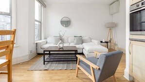 A modern living room with a sofa, coffee table, and a dining area with chairs. - Amazing Flat in Battersea (London)