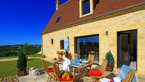 Ein Steinhaus mit gefliester Terrasse, Sitzgelegenheiten im Freien und Blick auf die Landschaft.