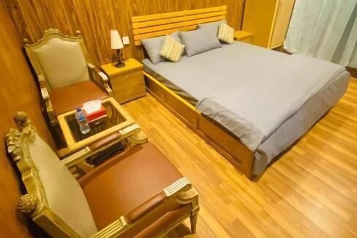 A wooden-paneled room with a bed, a nightstand, a chair, and a small table.