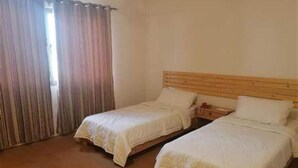Una habitación con dos camas individuales, un cabecero de madera y una ventana con cortinas.