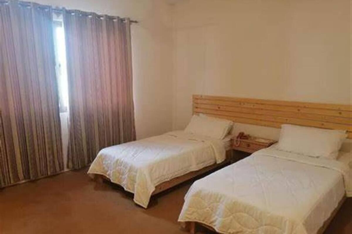 A room with two single beds, a wooden headboard, and a window with curtains.