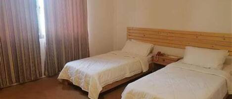 A room with two single beds, a wooden headboard, and a window with curtains.