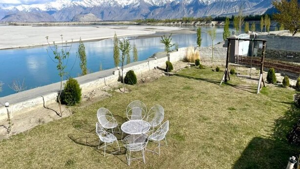 Un patio junto al lago con mobiliario exterior, un pequeño pabellón y vistas a montañas nevadas.