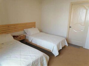A room with two single beds, a wooden headboard, a bedside table with a lamp, and a door with a decorative panel. - Indus View Hotel (Skardu)