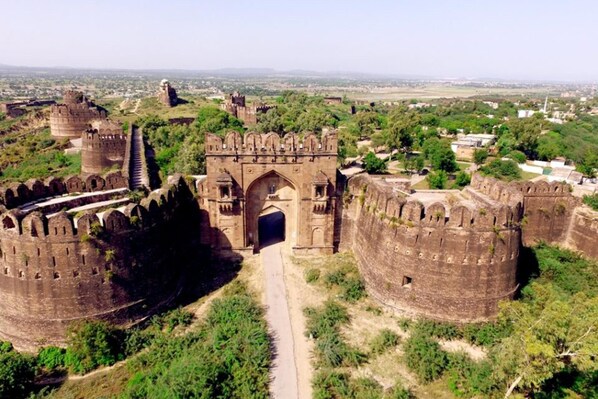 A historical fort with a large central gate, surrounded by high walls and smaller towers, set in a green landscape with distant buildings. - Inviting 3-bed House in Jhelum (Jhelum)