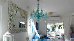 Uma sala de jantar com mesa azul e cadeiras brancas, um candelabro branco e um espelho grande com moldura floral.